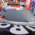 Com bandeiras e carros de som, o grupo se reuniu em frente ao prédio do Banco Central (BC), criticando o presidente da instituição, Campos Neto, durante o protesto. (Foto: Agência Brasil)